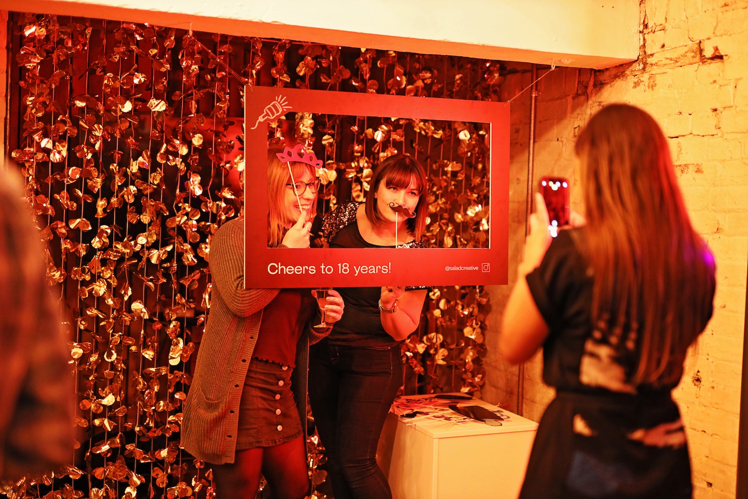 A woman taking a photo of two guests posing behind the photo frame